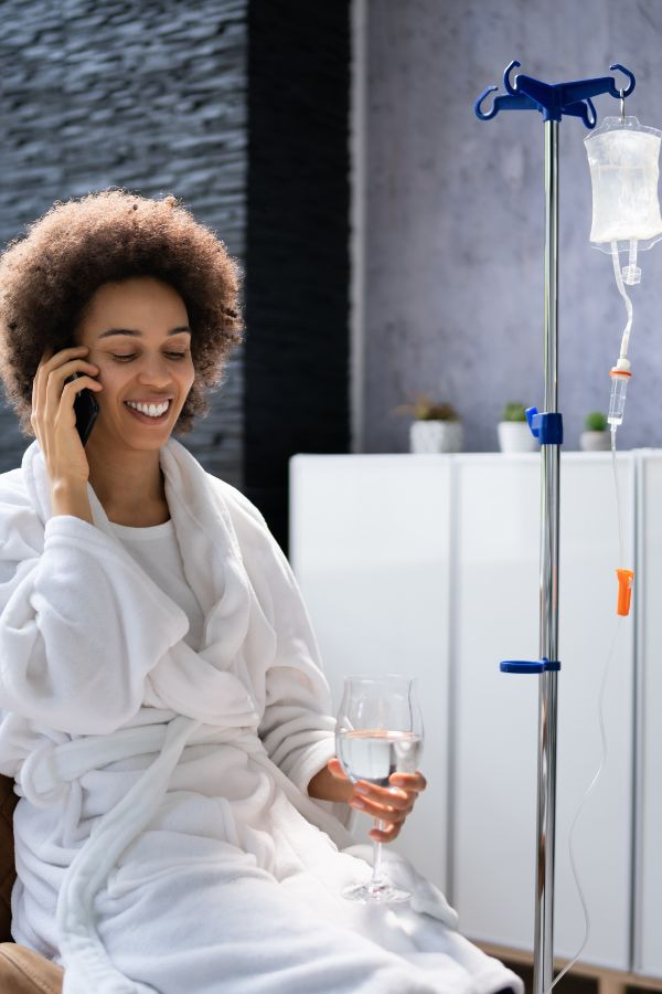 image of a woman smiling and talking on the phone while receiving IV therapy