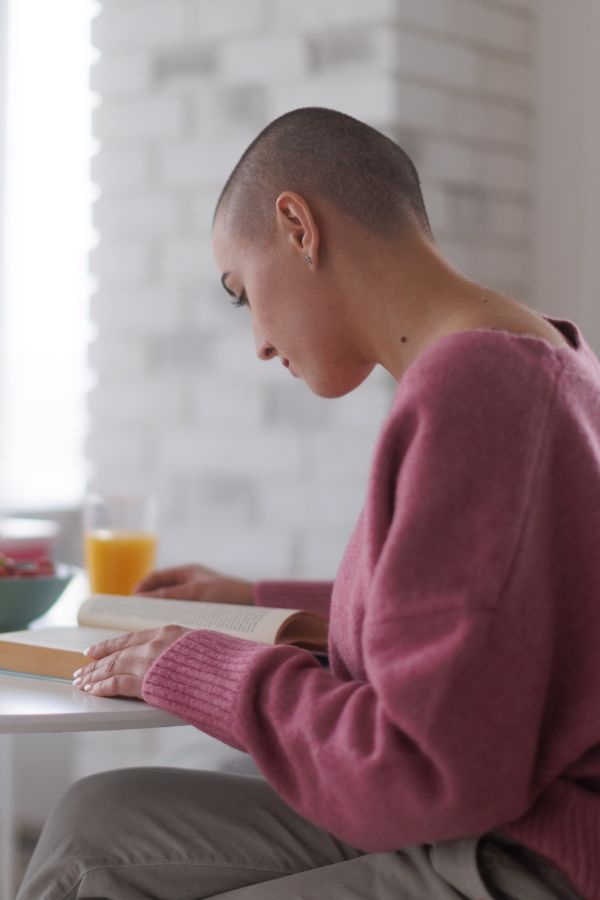 image of a woman with a shaved head sitting down and reading a book