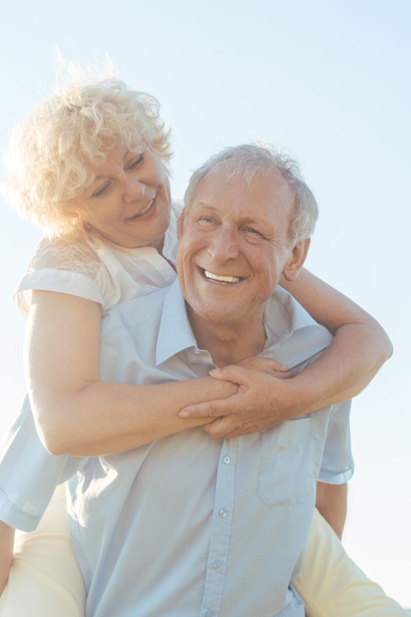 image of an elderly couple smiling and giving each other a piggyback ride