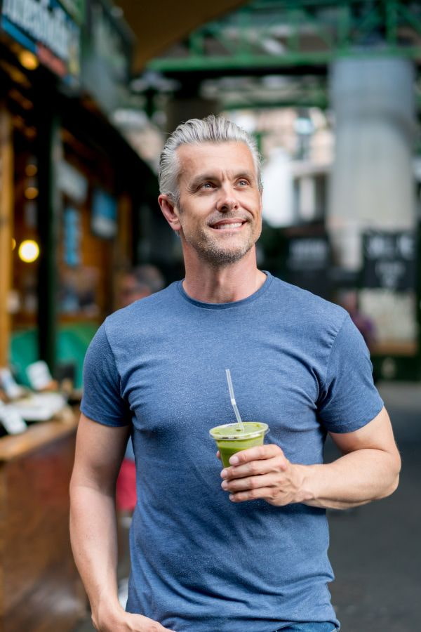 image of a man walking through a city while holding a cup of green juice
