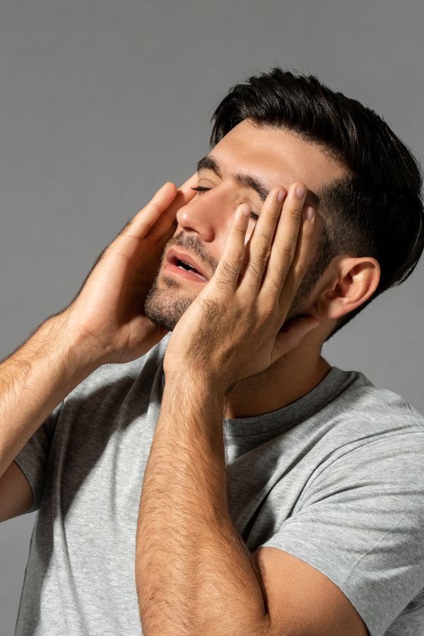 image of a fatigued man holding his face and looking into a light
